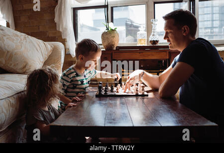 Seitenansicht des Vaters spielt Schach mit Kindern am Tisch zu Hause Stockfoto