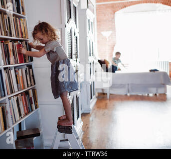 Seitliche Sicht auf Mädchen stehen Bücherregale Leiter mit Bruder im Hintergrund zu Hause Stockfoto