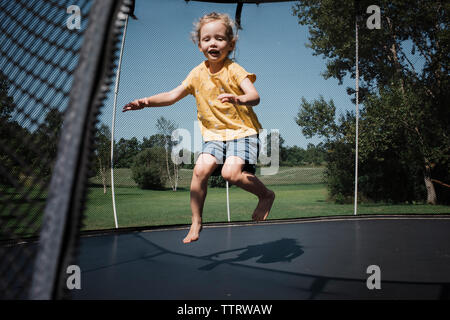 Portrait von süßen verspielten Mädchen springen auf Trampolin gegen den klaren Himmel im Park während der sonnigen Tag Stockfoto