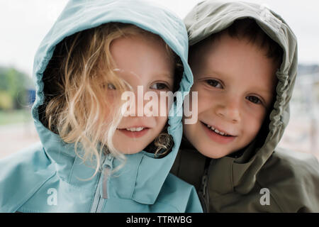 Close-up von lächelnden Geschwister in regenmäntel gegen Fenster zu Hause stehend Stockfoto