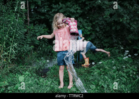 Die ganze Länge der Schwester gießt Wasser von gummimanschette während Bruder inmitten von Pflanzen im Park Stockfoto