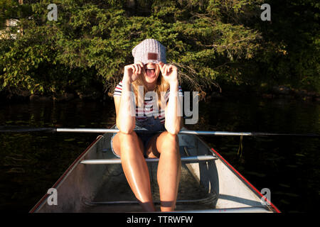 Glückliche Frau, Gesicht mit Stricken hat beim Sitzen im Boot auf dem Fluss gegen Bäume am Algonquin Provincial Park Stockfoto