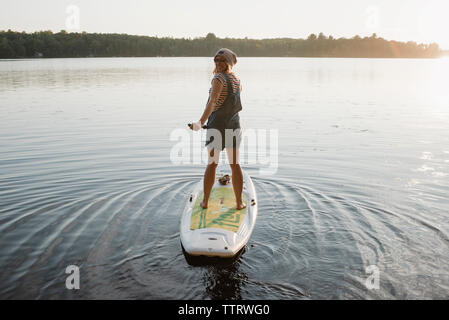 Portrait von Frau paddleboarding auf dem Fluss gegen Himmel bei Sonnenuntergang Stockfoto