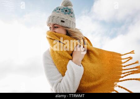 Blonde Frau hinter Schal am Strand lachend im Winter Stockfoto