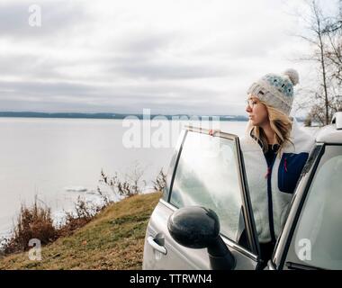 Blonde Frau, die mit dem Auto mit Blick auf das Wasser im Winter Stockfoto