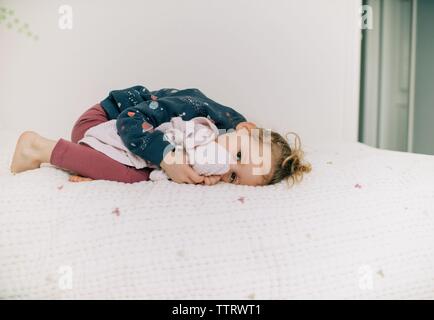 Junges Mädchen mit auf ihr Bett kuscheln Spielzeug Ihr daumenlutschen Stockfoto