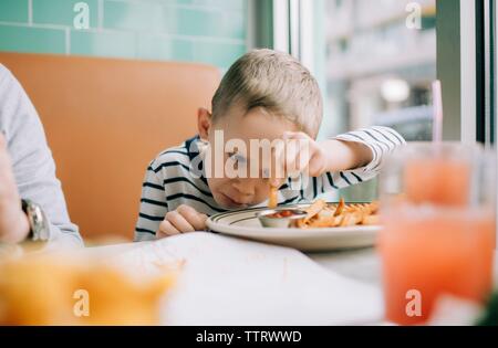 Junge Essen Pommes Eintauchen in Soße in einem Restaurant Stockfoto