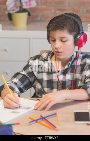 Junge Musik hören während der Färbung auf Buch mit Buntstift am Tisch in Home Stockfoto