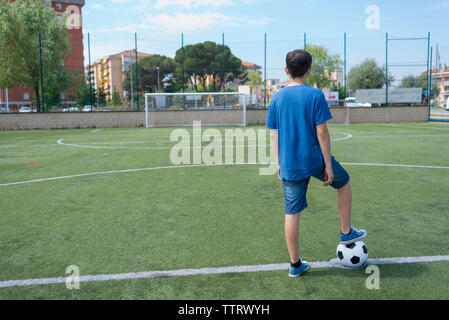 Ansicht der Rückseite des Junge spielt Fußball auf Feld gegen Sky Stockfoto