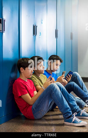 Schüler, die Smartphones benutzen, während sie auf dem Boden in der Umkleidekabine sitzen Stockfoto