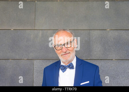 Portrait von zuversichtlich älterer Mann im Anzug gegen graue Wand stehend Stockfoto