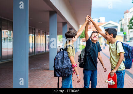 Gerne Freunde mit erhobenen Armen stehen auf Fußweg gegen Gebäude Stockfoto