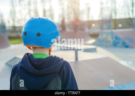 Ansicht der Rückseite des Jungen mit blauen Helm im Skatepark Stockfoto