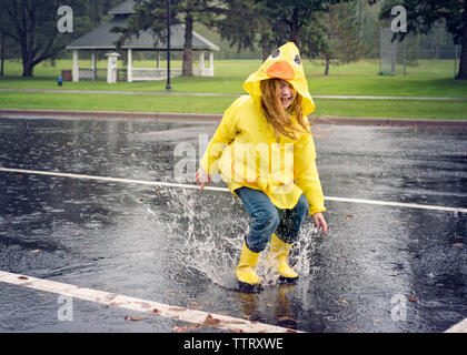 Verspielte Mädchen Regenjacke tragen beim Springen in der Pfütze bei Regen Stockfoto