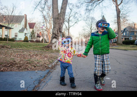 Geschwister halten sich an den Händen, während durch ein Fernglas schauen, beim Spielen auf der Straße Stockfoto