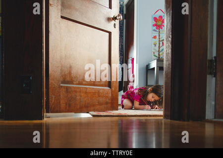 Mädchen mit Hausaufgaben, während auf dem Teppich durch die Tür zu Hause gesehen sitzen Stockfoto