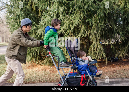 Seitenansicht des Vaters drücken Kinder sitzen auf Baby Stroller im Park Stockfoto