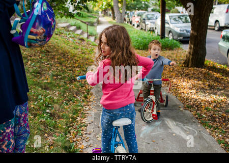 Mittelteil der Mutter halten Helm, während die Kinder auf dem Fahrrad über Wanderweg im Herbst Stockfoto