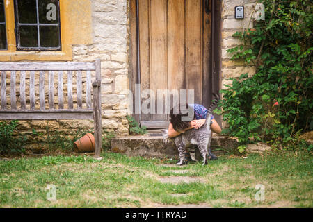 Junge Katze streicheln, während sie von Cottage im Hof sitzen Stockfoto