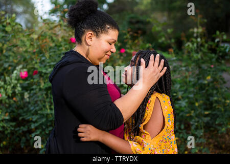 Seitenansicht von Mutter und Tochter sich einander beim Stehen gegen Pflanzen im Park Stockfoto