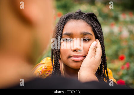 Zugeschnittenes Bild der Mutter mit der Hand am Kinn ständigen's Tochter in Park Stockfoto