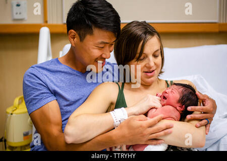 Stolz neue Eltern Wiege ihre lächelnden Neugeborenen in einem Krankenhausbett Stockfoto