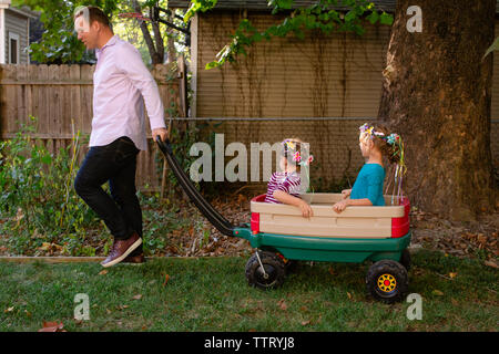 Ein glücklicher Vater zieht seine zwei kleinen Mädchen in einem Wagen in Ihrem Garten Stockfoto