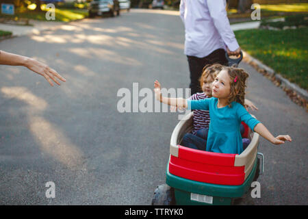 Eltern zu Fuß die Straße runter ziehen zwei kleine Mädchen in einem Wagen Stockfoto