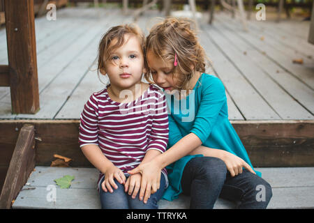 Zwei kleine Mädchen halten Sie Hände und Lean in der Nähe sitzen zusammen auf dem Deck Stockfoto