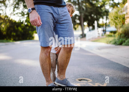 Portrait von ein schüchterner kleiner Junge spähen hinter Beine seines Vaters Stockfoto