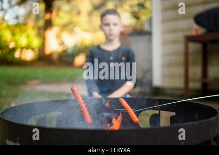 Ein Junge rösten Hot Dogs mit seiner Familie auf einer Feuerstelle im Freien Stockfoto