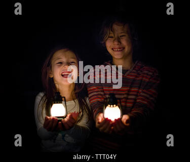 Zwei lachende Kinder stehen im Schatten halten kleine Laternen in den Händen Stockfoto