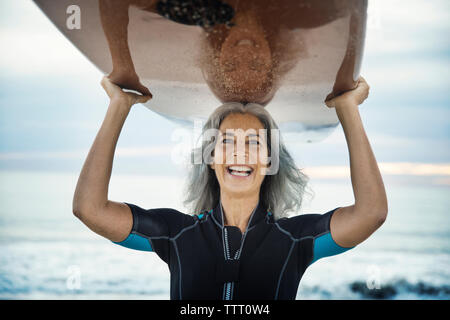 Portrait von Happy weibliche surfer Surfbrett tragen auf dem Kopf in Delray Beach Stockfoto