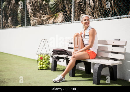 Volle Länge des lächelnden reife Frau am Tennisplatz sitzen Stockfoto