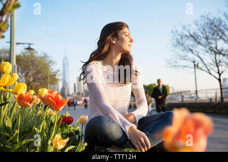 Nachdenkliche Frau sitzt auf der Stützmauer mit One World Trade Center im Hintergrund Stockfoto