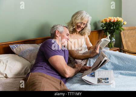 Fröhliche Frau mit Buch Mann, während auf dem Bett zu Hause sitzen Stockfoto