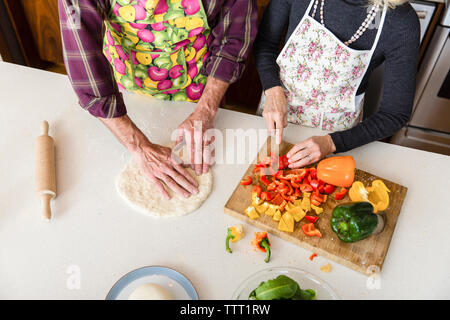 Mittelteil der Frau schneiden Paprika, während Mann, Pizza Teig in der Küche zu Hause. Stockfoto