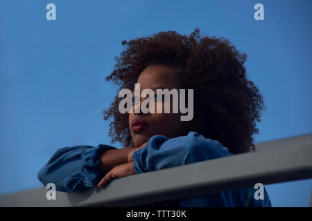 Low Angle View von nachdenklich Frau lehnte sich auf Geländer gegen den klaren blauen Himmel Stockfoto