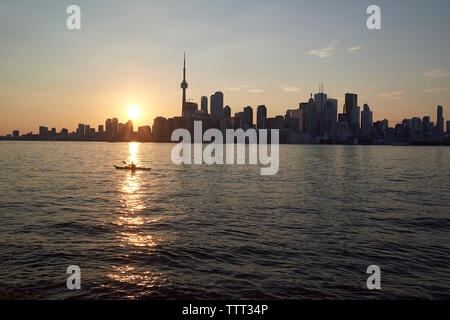 Silhouette modernen Gebäuden, die durch Fluss gegen Himmel bei Sonnenuntergang Stockfoto