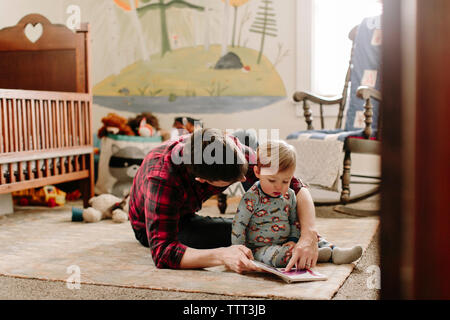 Vater zeigt Bild Buch zum Sohn, während zu Hause sitzen Stockfoto