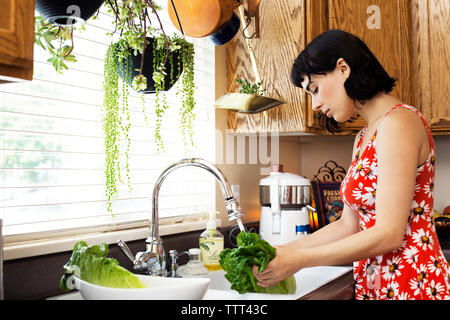 Seitenansicht der Frau Waschen von Salat in der Küche Stockfoto