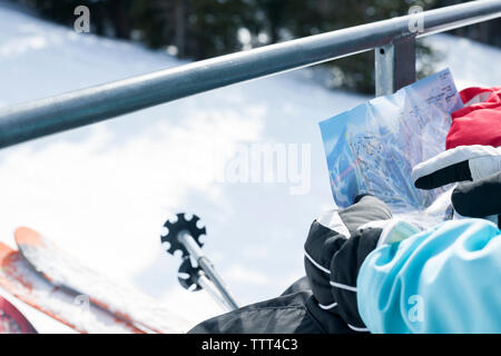 Zugeschnittenes Bild von Mädchen auf Karte suchen, beim Reiten auf Skilift Stockfoto