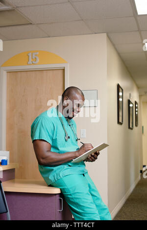 Männlicher Arzt schriftlich beim Schiefen auf Tisch im Flur Stockfoto