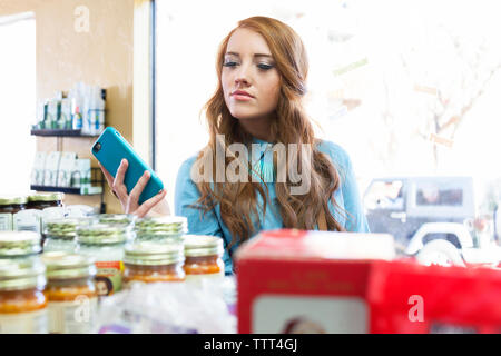 Frau mit Mobiltelefon und Lebensmittel in Store suchen Stockfoto