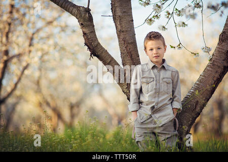 Portrait von süßen Jungen mit Händen in den Taschen gegen den Baumstamm am Bauernhof stehend Stockfoto