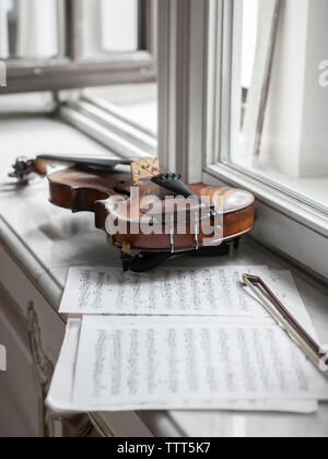 Hohe Betrachtungswinkel der Violine mit Noten und Bug auf der Fensterbank im Herrenhaus Stockfoto