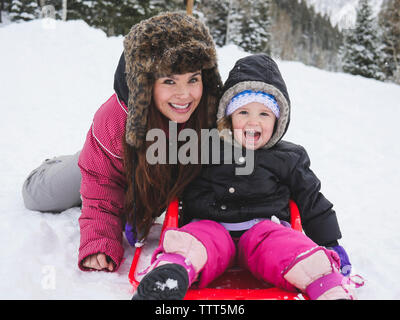 Portrait der glücklichen Mutter mit Tochter sitzen auf schneebedeckten Feld Stockfoto