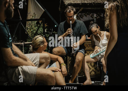 Mann und Frau die Musikinstrumente beim Sitzen mit Freunden im Resort Stockfoto
