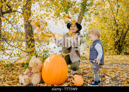 Glückliche Mutter und Sohn spielen mit Blätter im Herbst im Park während der Halloween Stockfoto