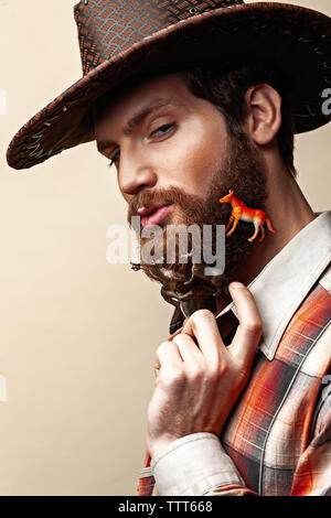 Junger Mann in einem Cowboyhut und Spielzeug Pferde in einen Bart Stockfoto